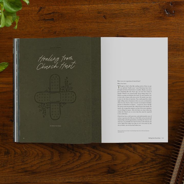 An open magazine spread laid flat on a wooden table. The left page is dark olive green with the title 'Healing from Church Hurt' in white script and a cross-shaped illustration.