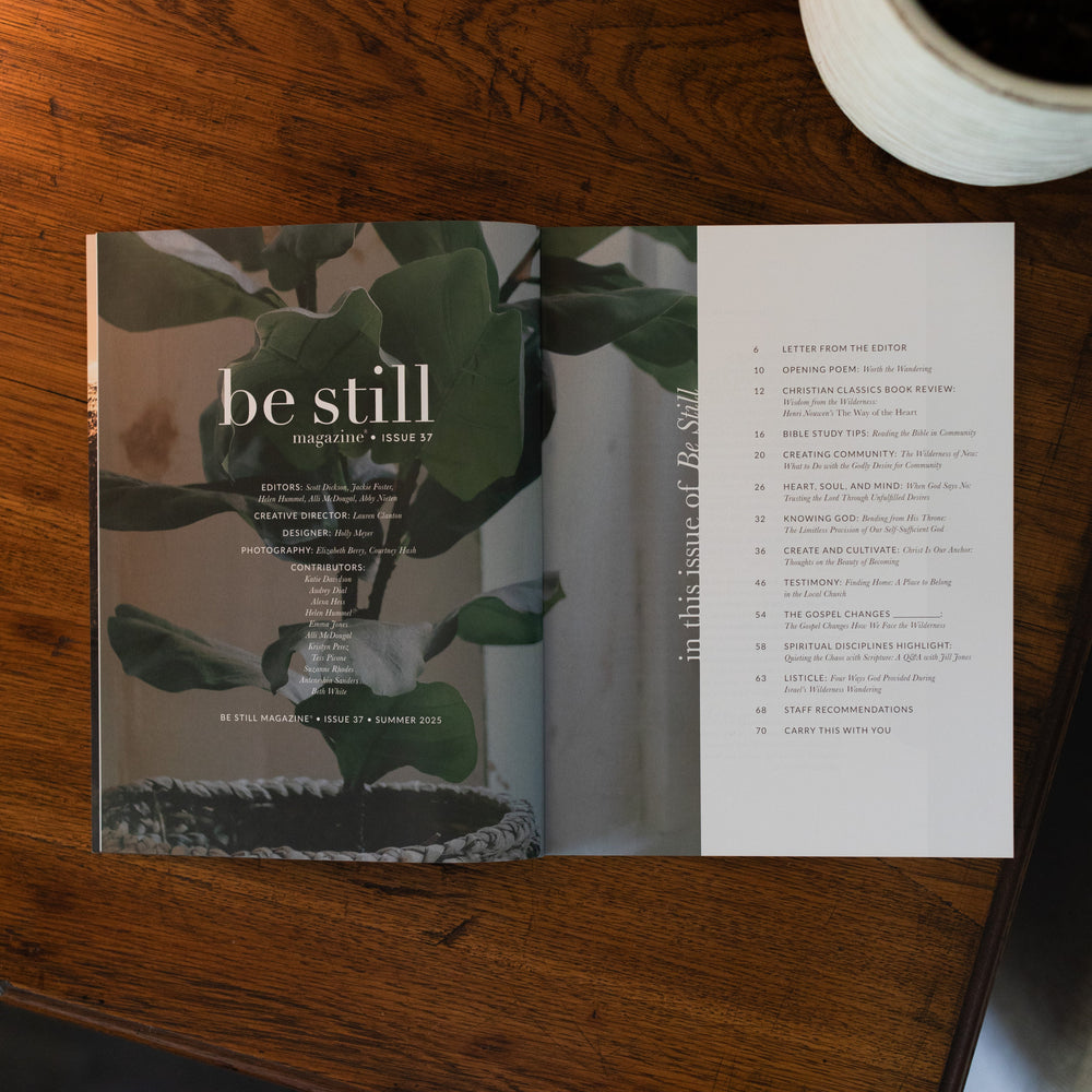 Be Still Issue 37 Magazine opened to the table of contents page on a brown wooden table next to a white potted plant