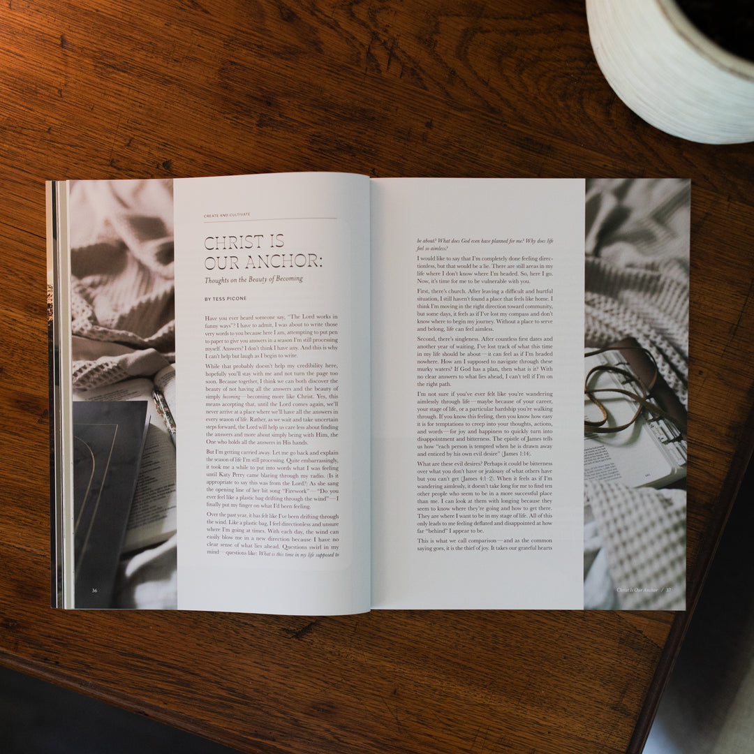 Be Still Issue 37 Magazine opened to the christ is our anchor page on a brown wooden table next to a white potted plant