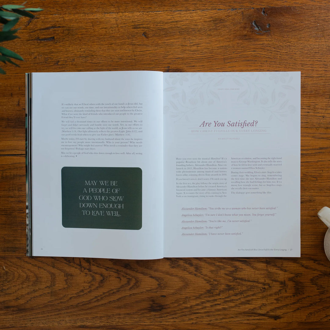 Be Still Magazine Issue 39 opened to the Are you Satisfied page on a wooden table next to a coffee cup