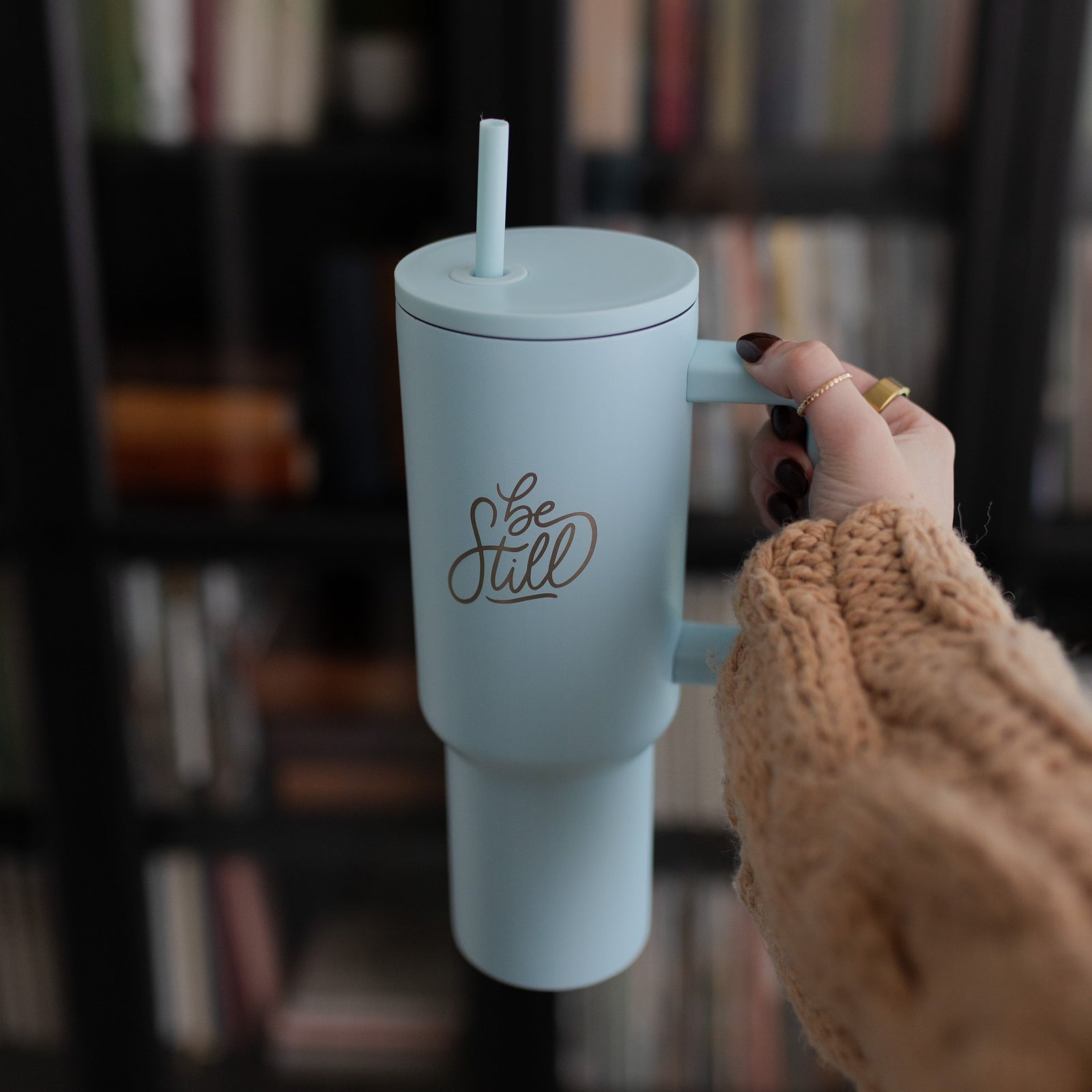 Woman holding Christian tumbler with straw that says Be Still.