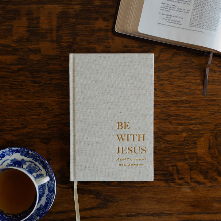 Be With Jesus Lent Prayer Journal cover on a wooden table next to an open bible and a tea cup