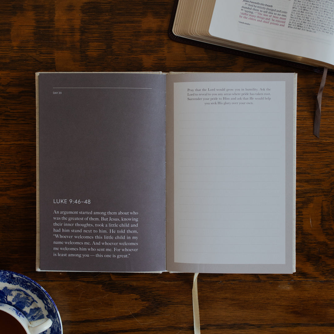 Be With Jesus Lent Prayer Journal opened to the Luke 9:46 questions page on a wooden table next to an open bible and a tea cup