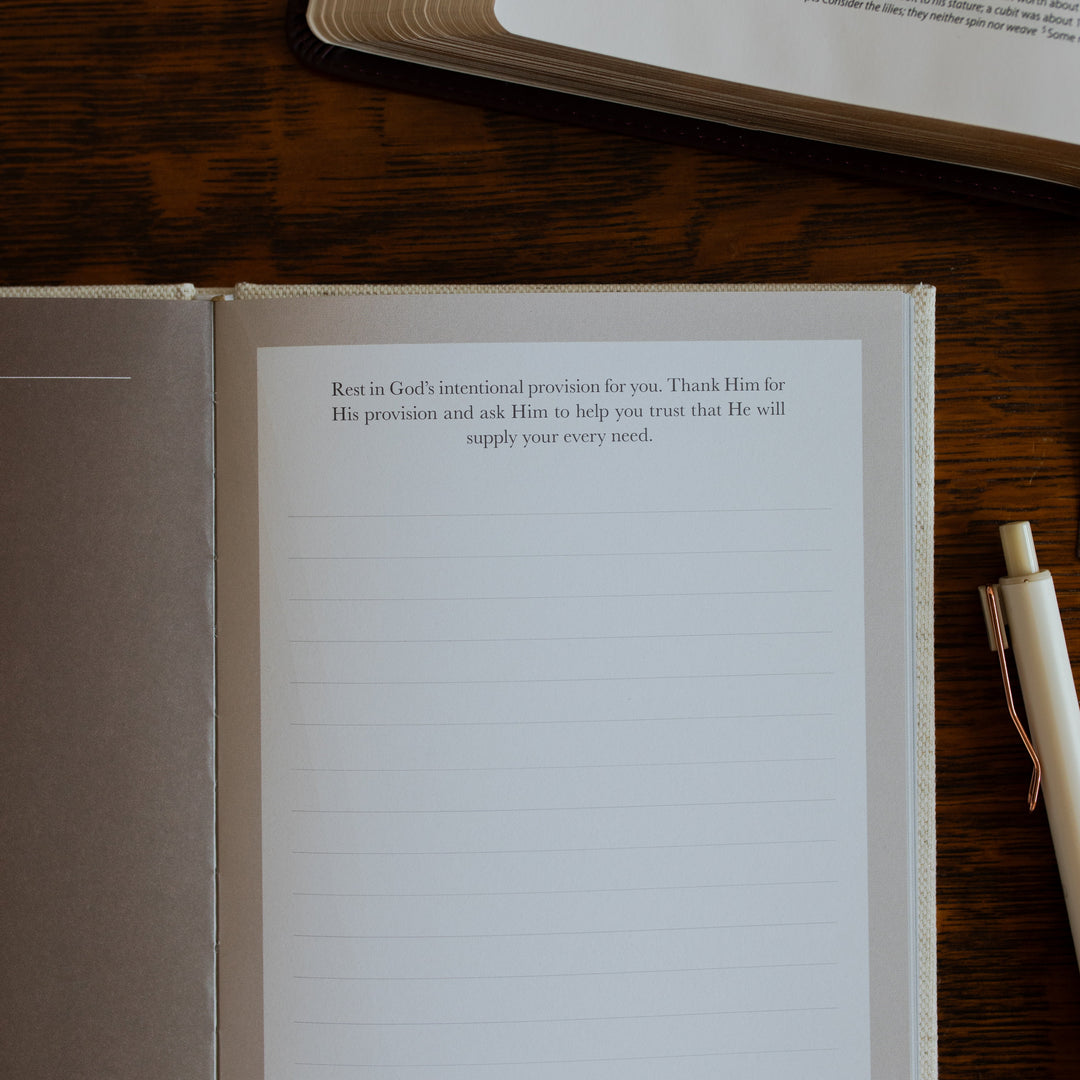 Up close of the Be With Jesus Lent Prayer Journal opened to a prayer page page on a wooden table next to an open bible