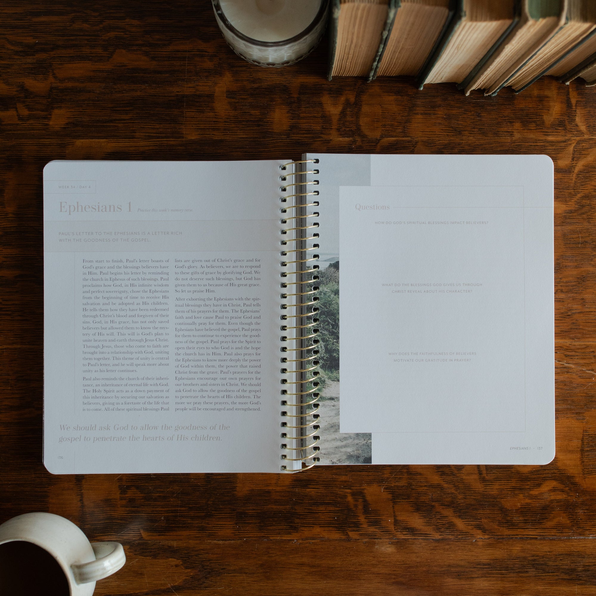 Behold Spiral opened to the Ephesians 1 questions page on a wooden table next to a coffee cup and some books