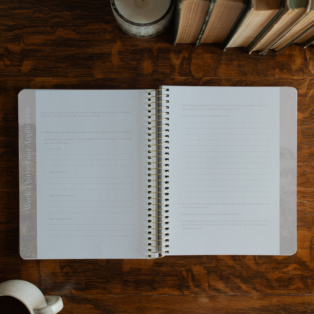 Behold Spiral opened to the applications page on a wooden table next to a coffee cup and some books