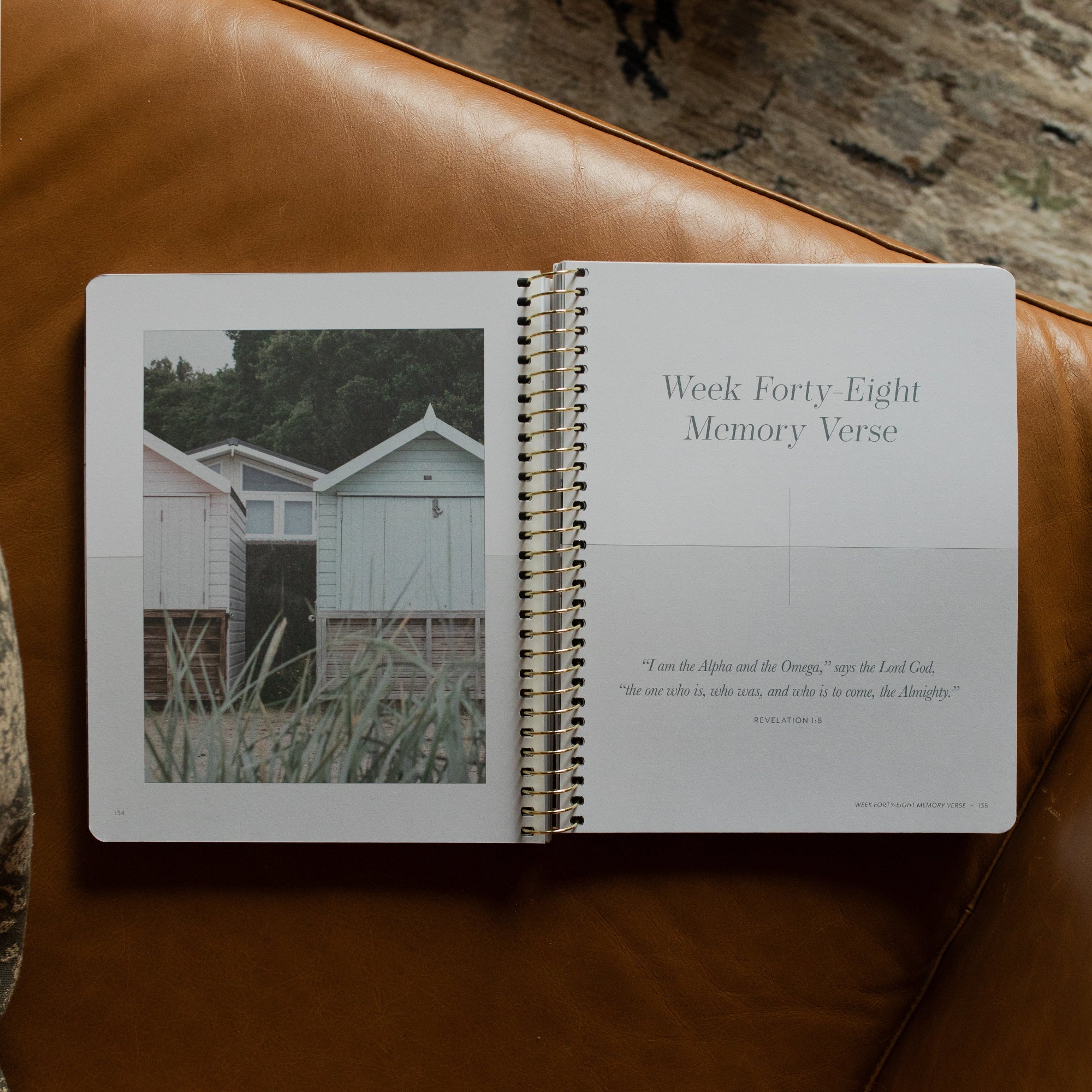 Behold Spiral Study opened to the Week Forty eight memory verse page on a leather couch