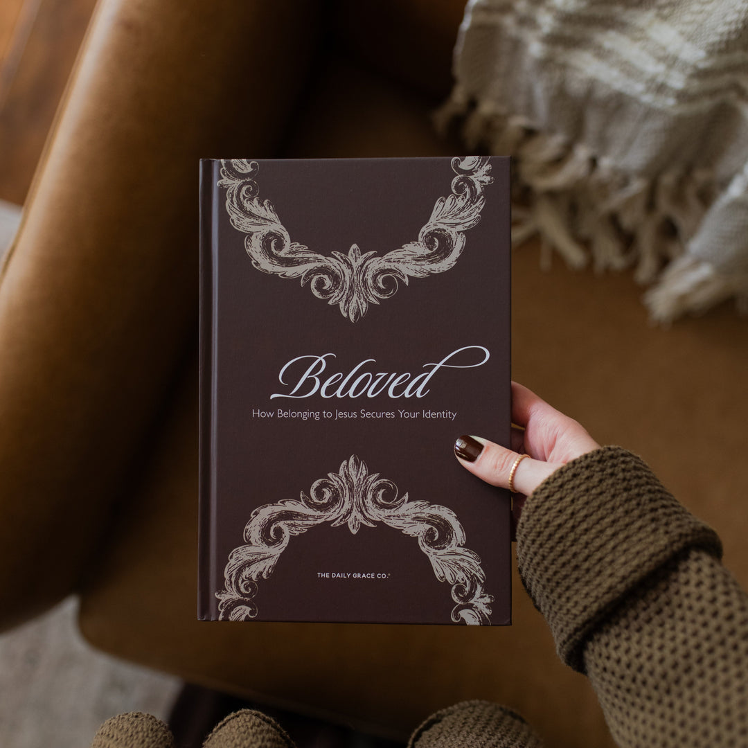 A woman holding the Beloved How Belonging to Jesus Secures your Identity book cover over a brown leather couch