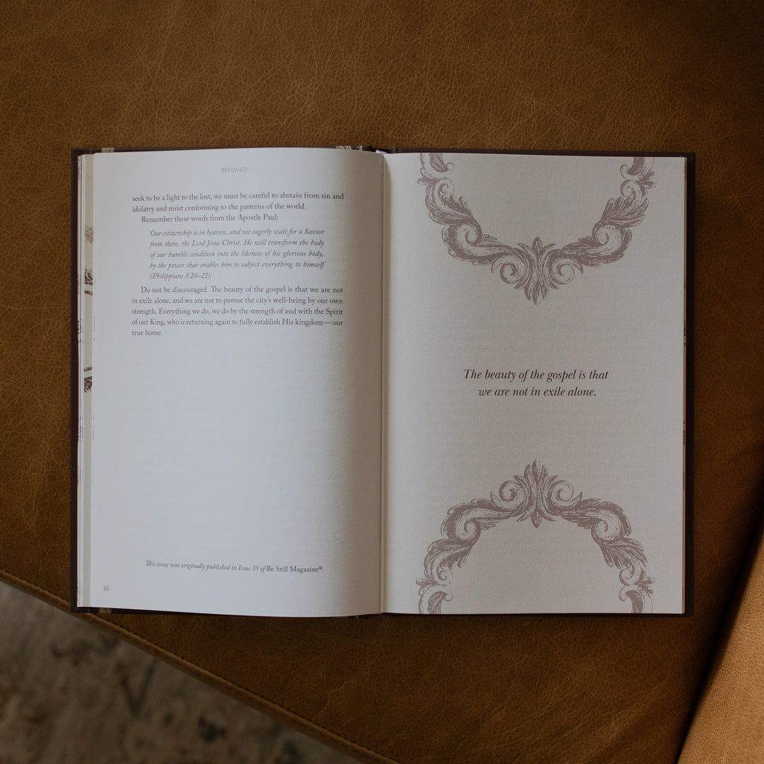 The Beloved How Belonging to Jesus Secures your Identity book opened to the the beauty of the gospel is that we are not in exile alone page resting on a brown leather couch