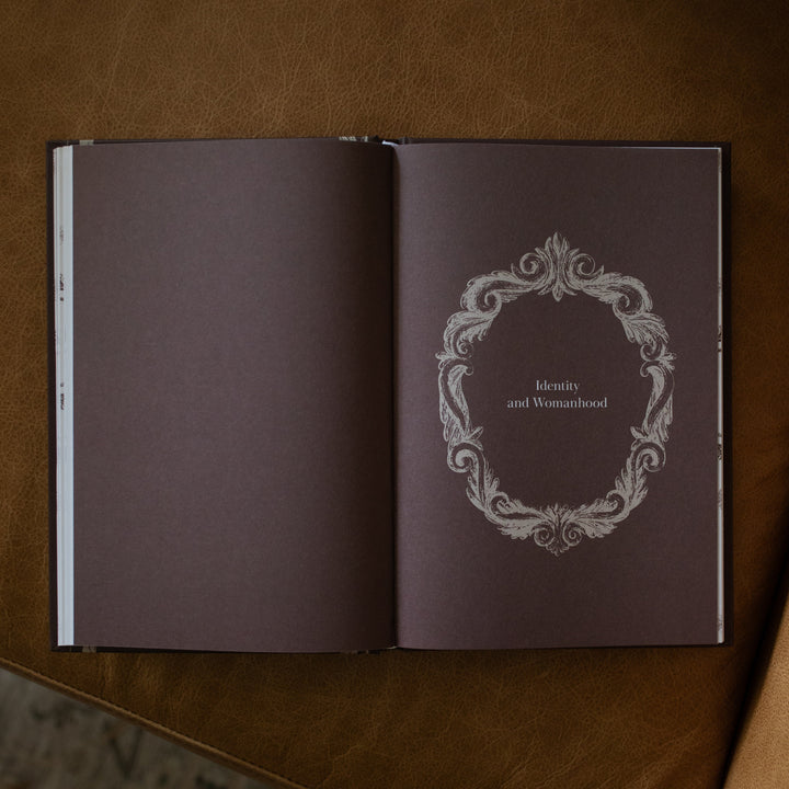 The Beloved How Belonging to Jesus Secures your Identity book opened to the Identity and Womanhood page resting on a brown leather couch