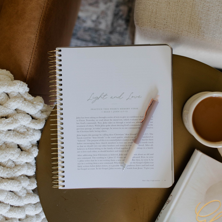 A notebook and pen beside a steaming cup of coffee on a wooden table, creating a cozy workspace atmosphere