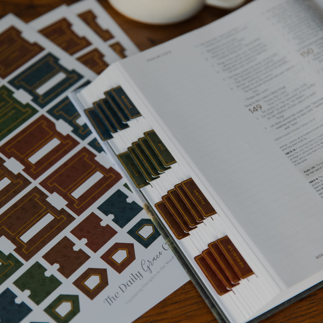 An open book or booklet on a wooden surface, showing printed interior plan diagrams and small colored tabs labeled with room names such as kitchen, bath, and closet. A matching printed sheet lies beside it.