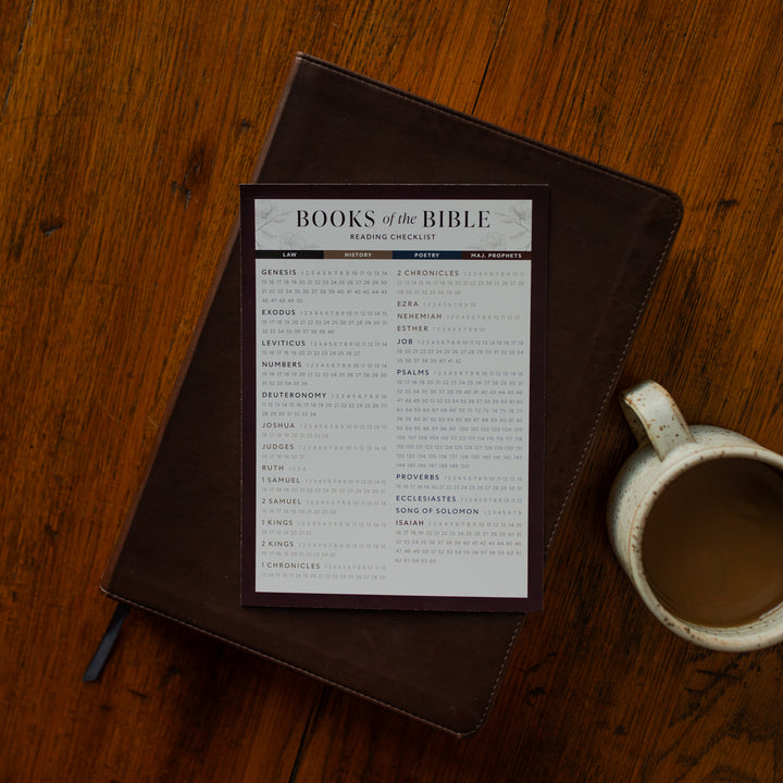 The Books of the Bible Checklist on a closed bible near a coffee cup