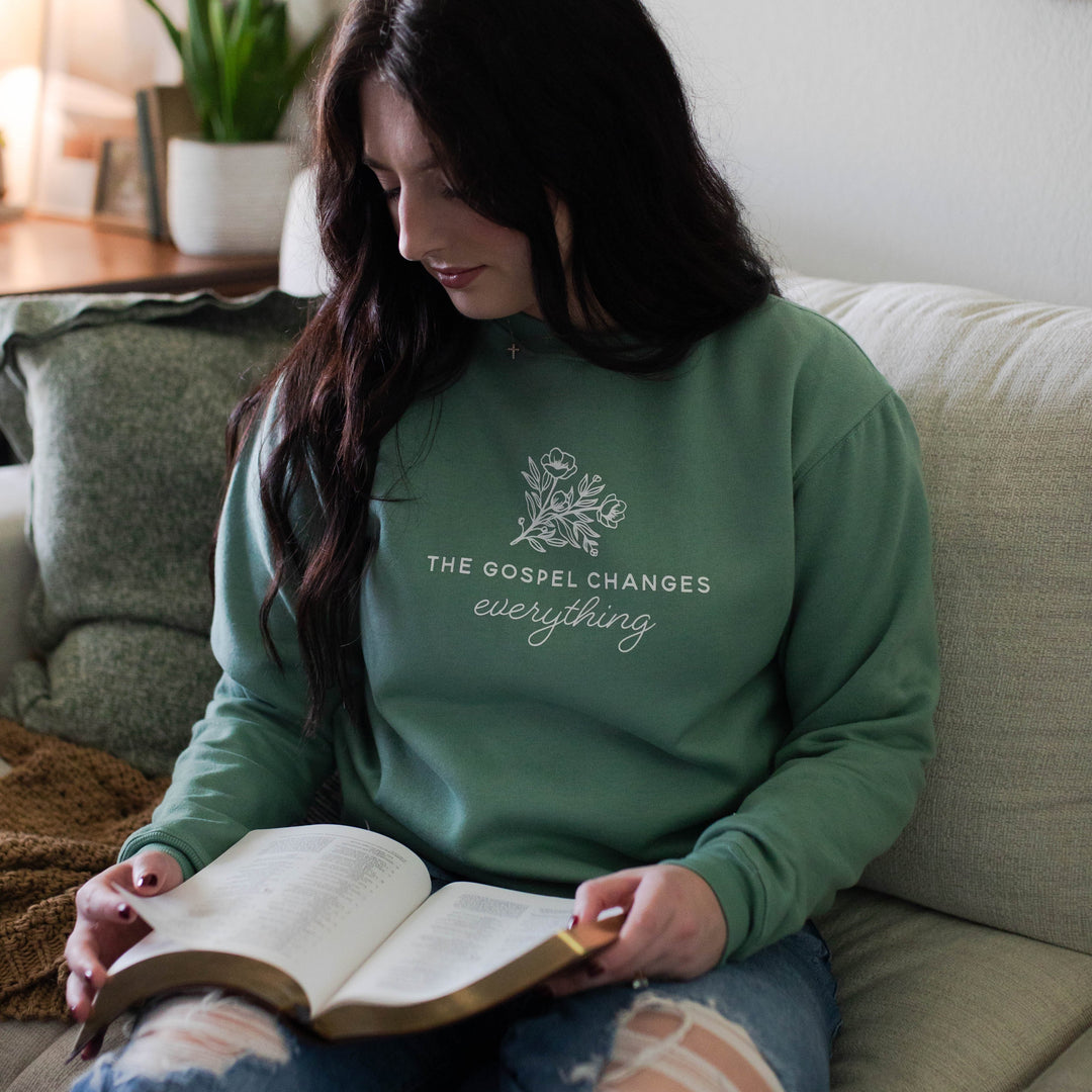 Woman wearing a green shirt that has a flower on it, reading a book.