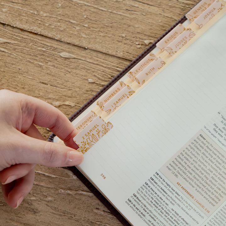 Hand holding a decorative bookmark in an open book on a wooden surface