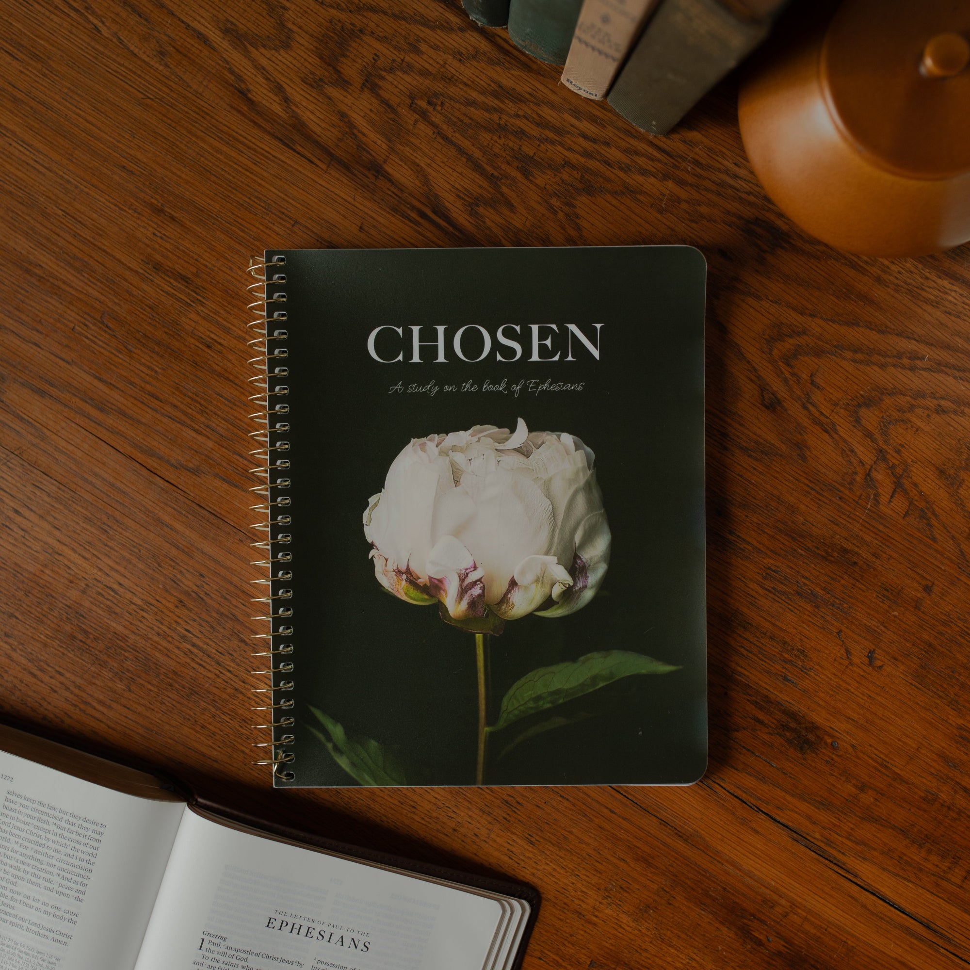 Spiral labeled Chosen with a white rose on the cover on a wooden table next to an open bible