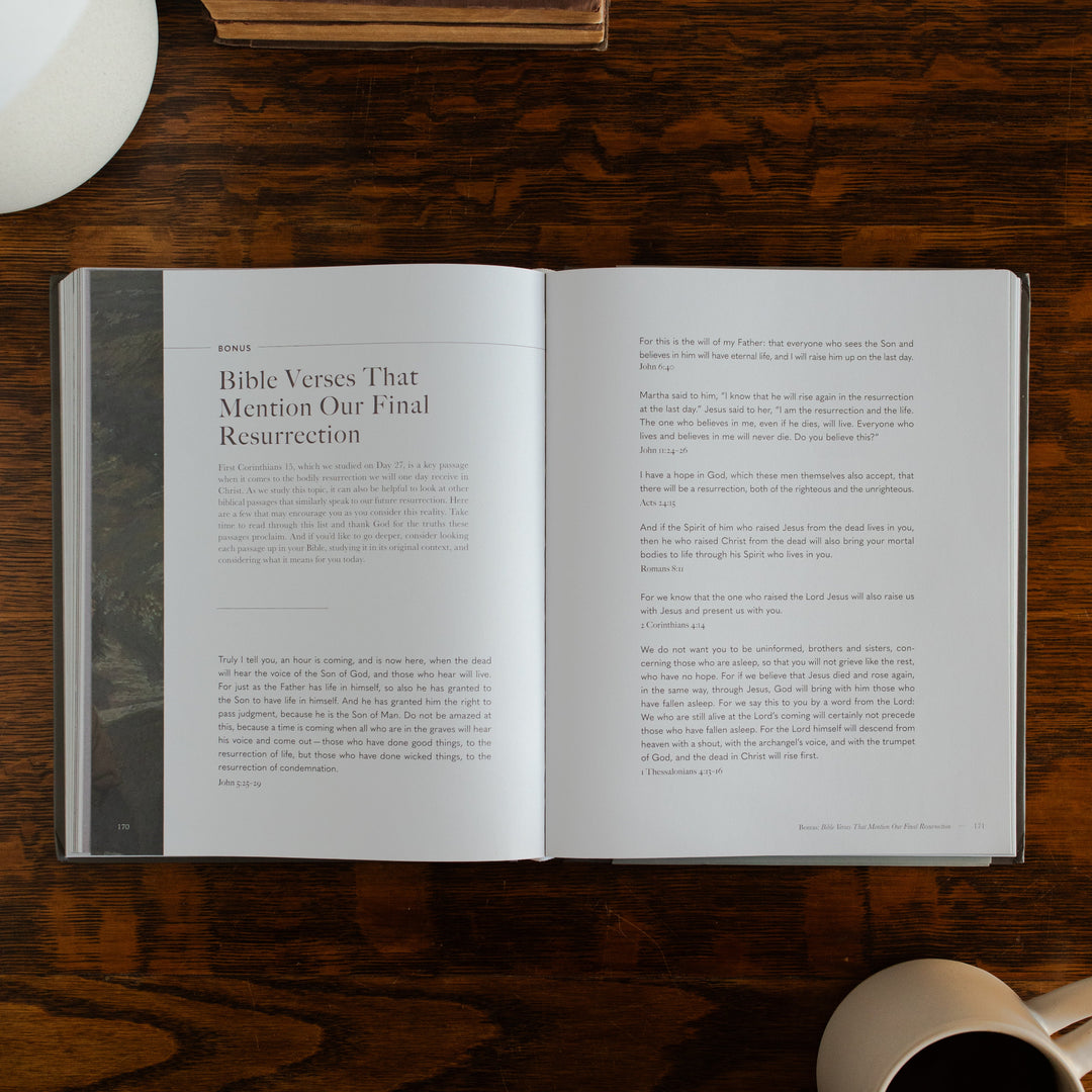 Clinging to the Cross Spiral hardcover opened to the bonus bible verses page on a wooden table next to a coffee cup