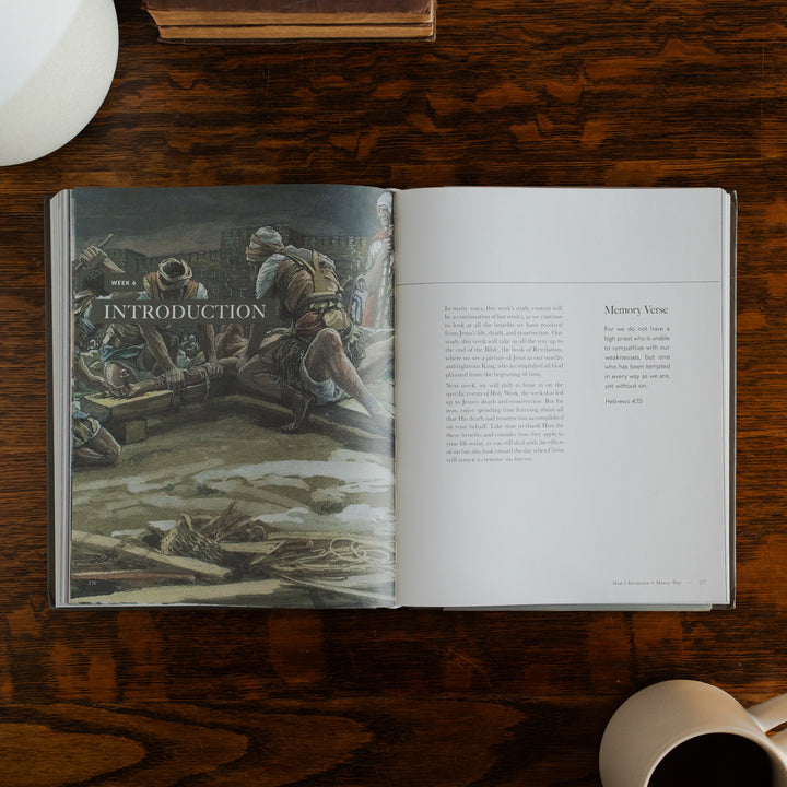 Clinging to the Cross Spiral hardcover opened to the introduction page on a wooden table next to a coffee cup