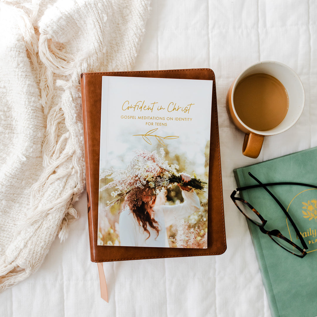 Book  titled 'Confident in Christ' on a white surface with a cup of tea and glasses.