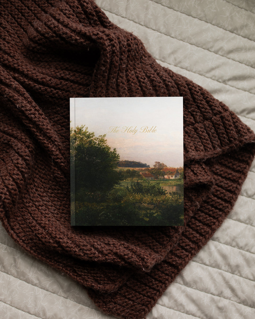 Book titled 'The Holy Bible' on a brown knitted blanket with a scenic cover