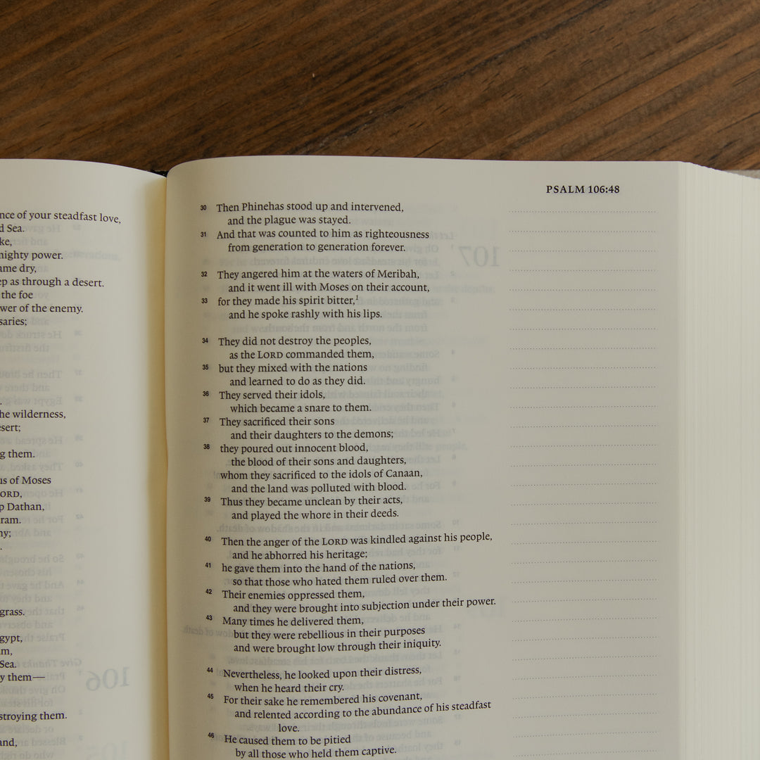 An open bible showing printed text from Psalm 106:48 on both pages, placed on a dark wood surface.