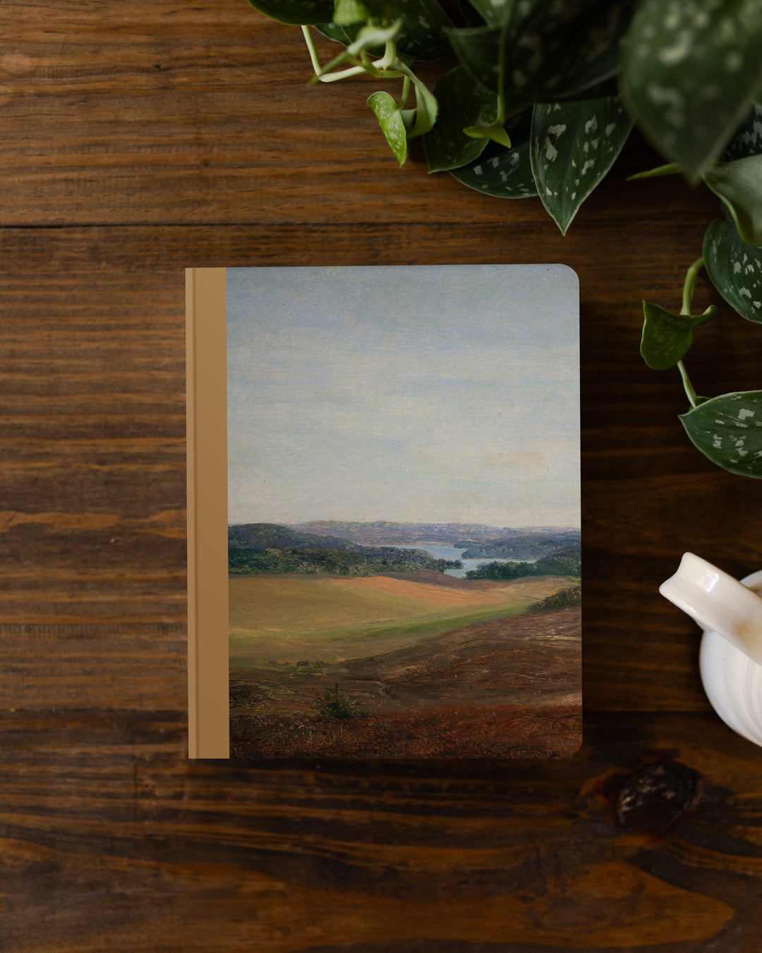 Notebook with a landscape design on a wooden surface with plants.