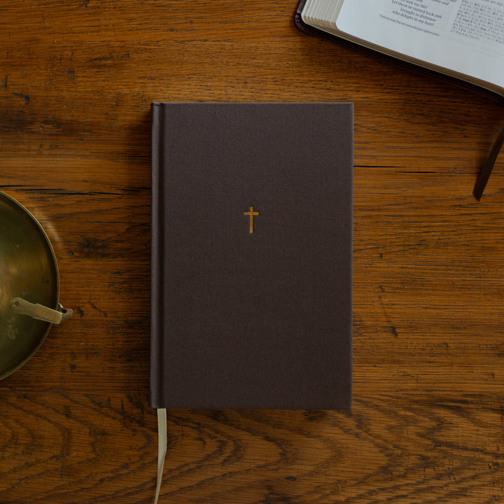 The Cross Journal cover next to an open bible and on a wooden table