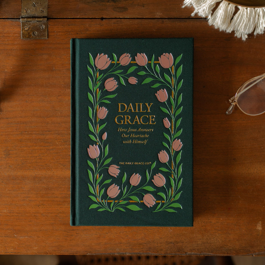 The Daily Grace Hardcover book cover on a wooden desk near a pair of glasses