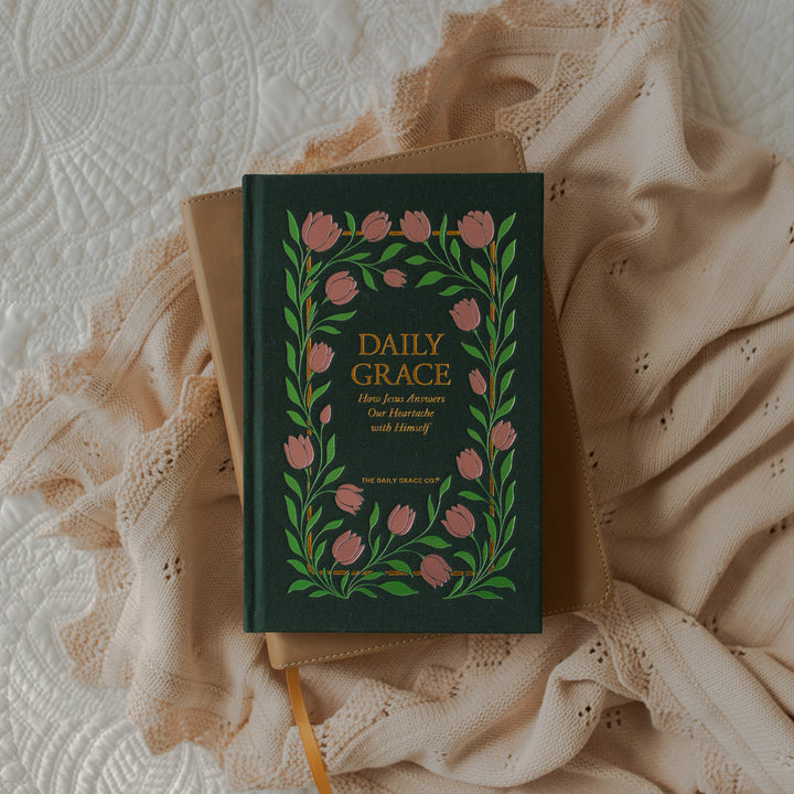 The Daily Grace Hardcover book cover on a closed bible on white sheets and a blanket