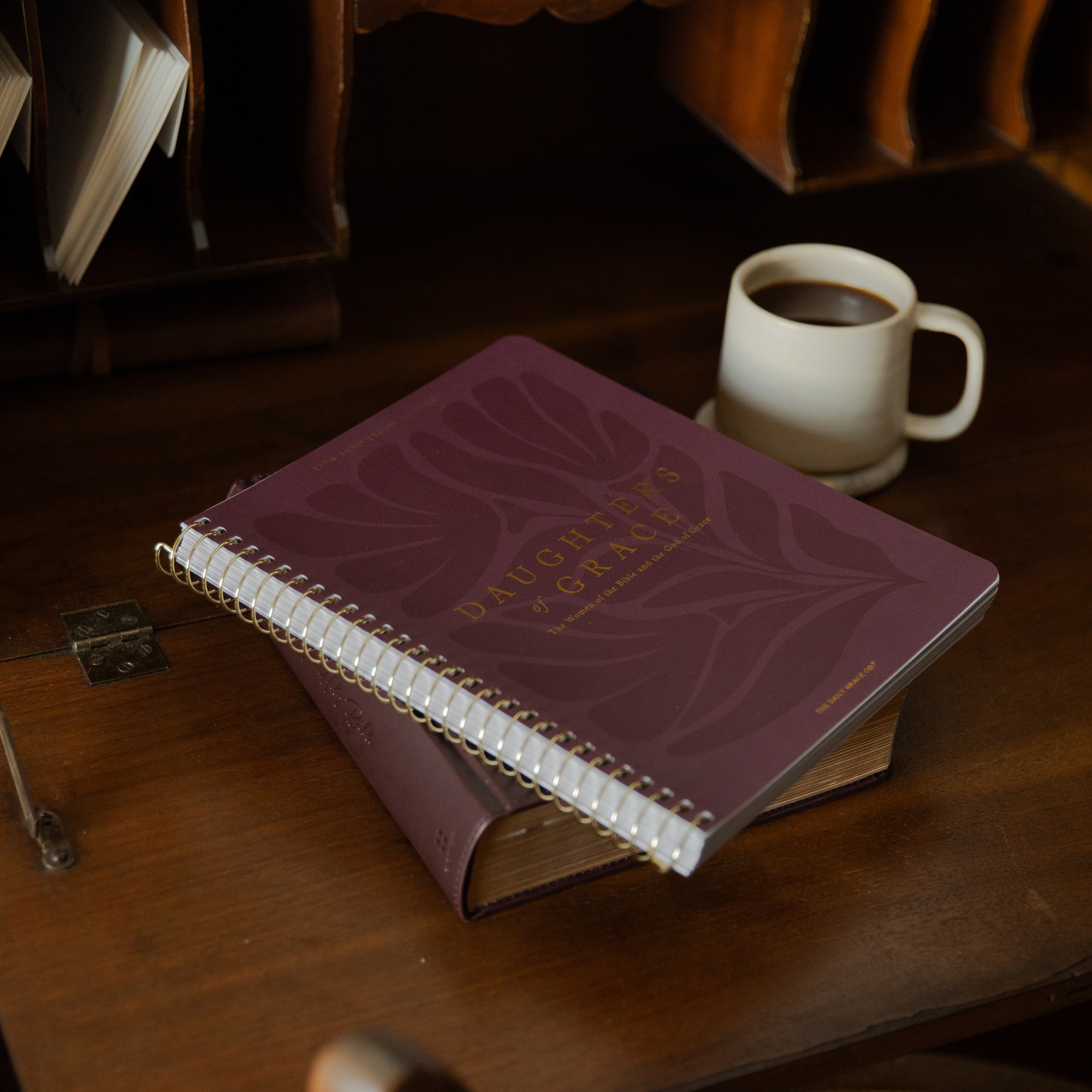 Purple Bible Study with white pages on a wooden table next to a cup of coffee.