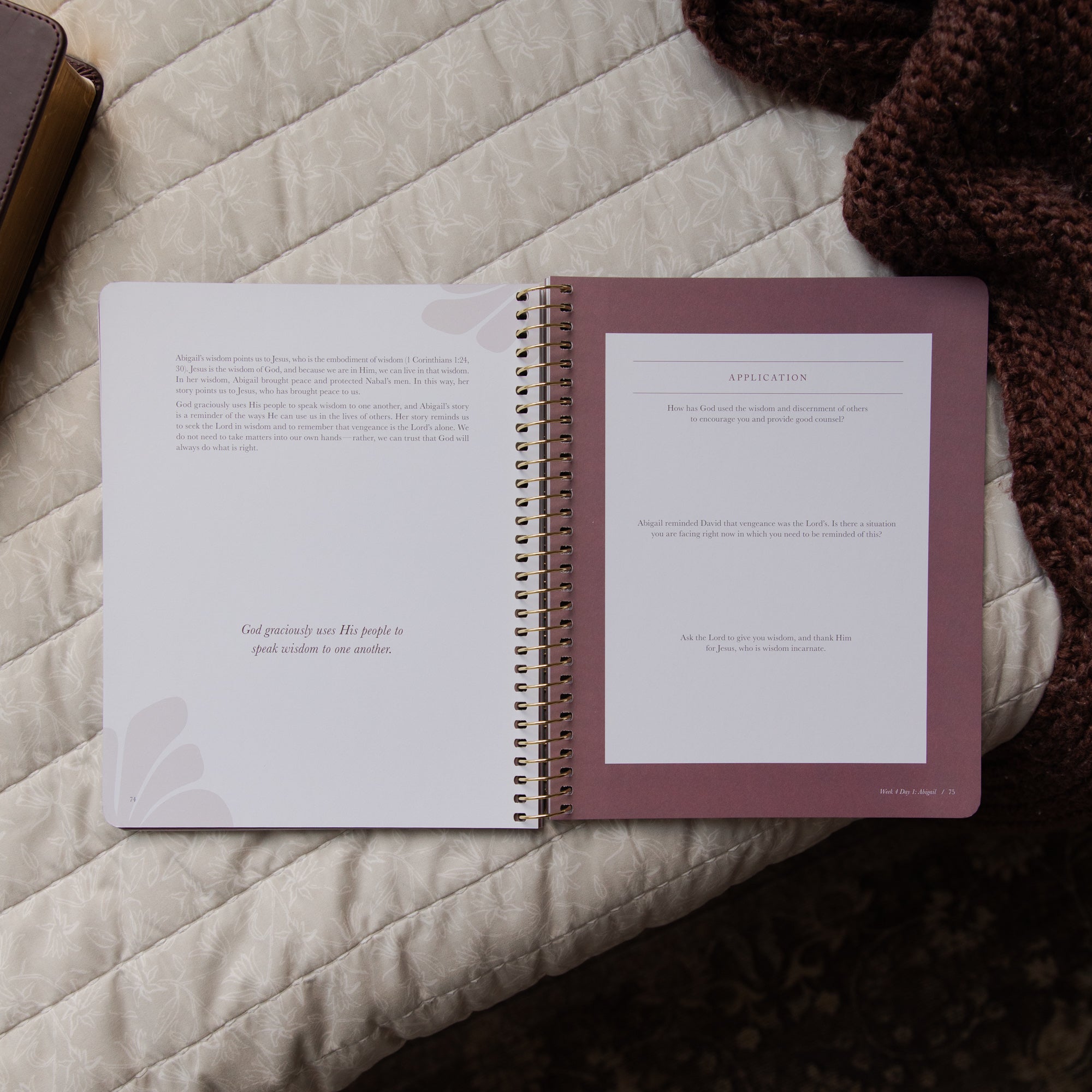 Open spiral-bound bible study on a textured surface with a brown knitted blanket.