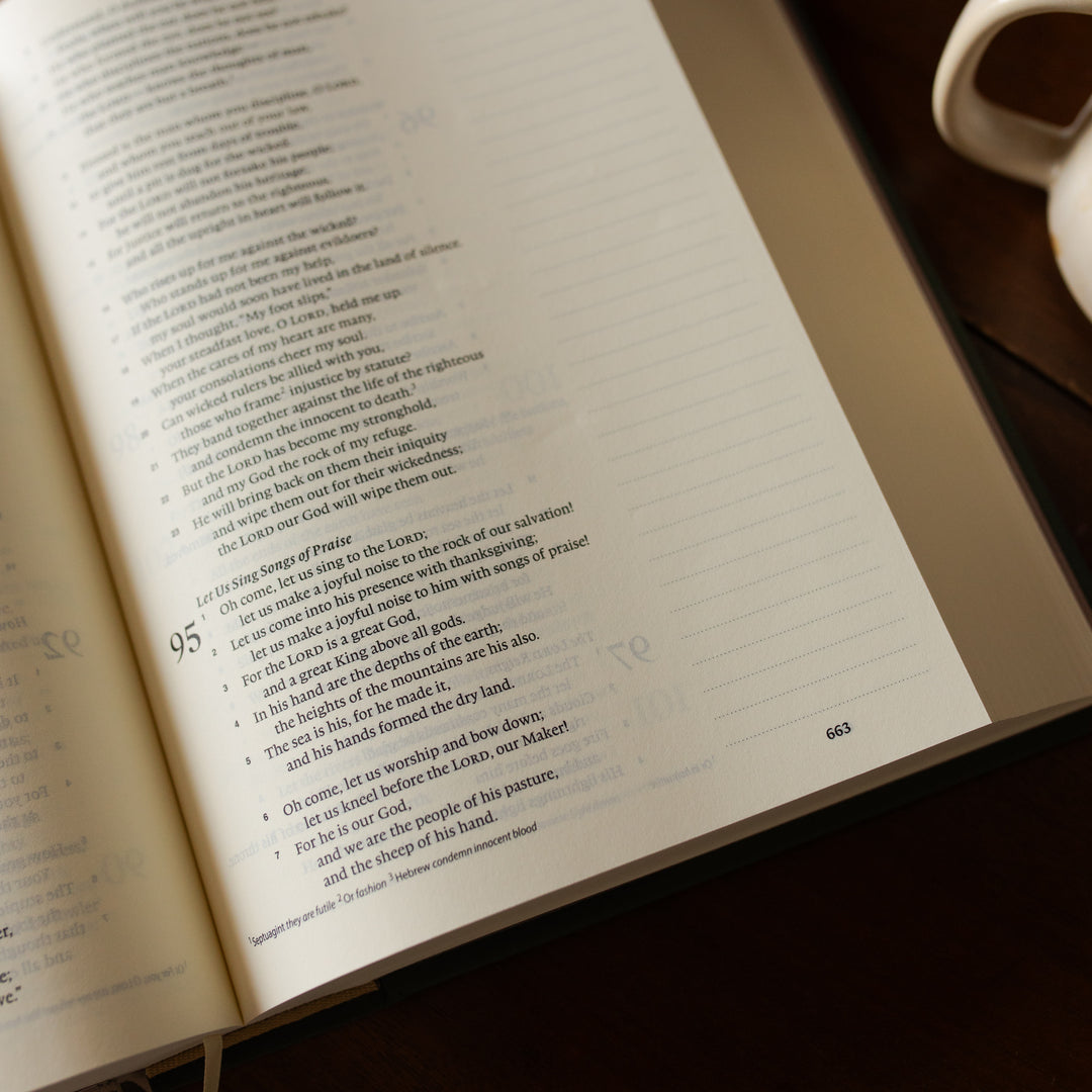 The Clover Journaling Bible opened with text on a wooden surface next to a white mug.