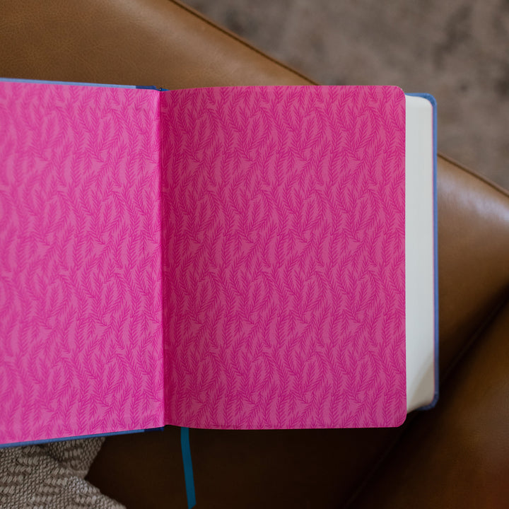 ESV Garden Bible opened to the first page, layered with pink and dark pink leaves while the bible is laying on a leather couch