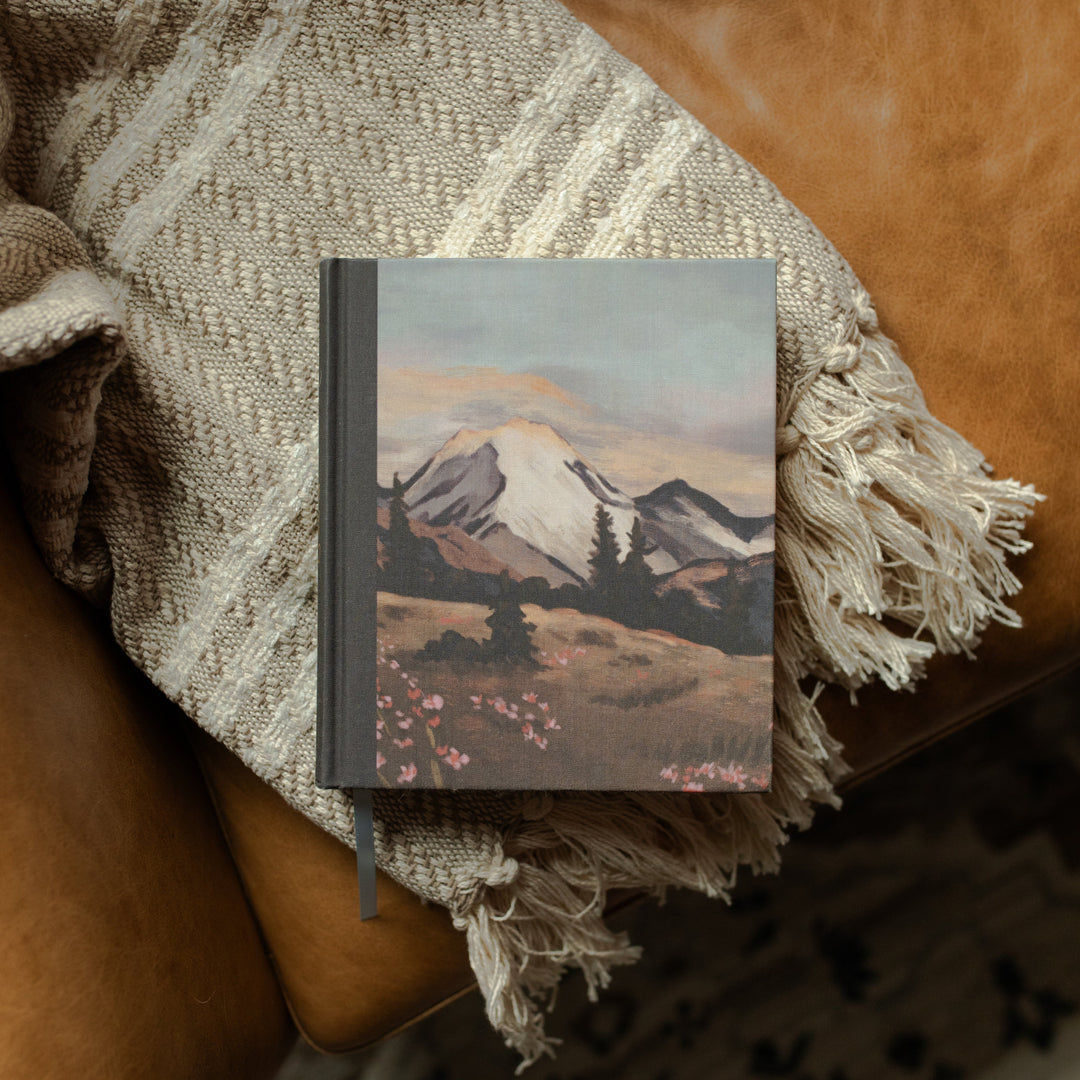 ESV Journaling Bible with mountains on the cover on a woven blanket and a leather couch