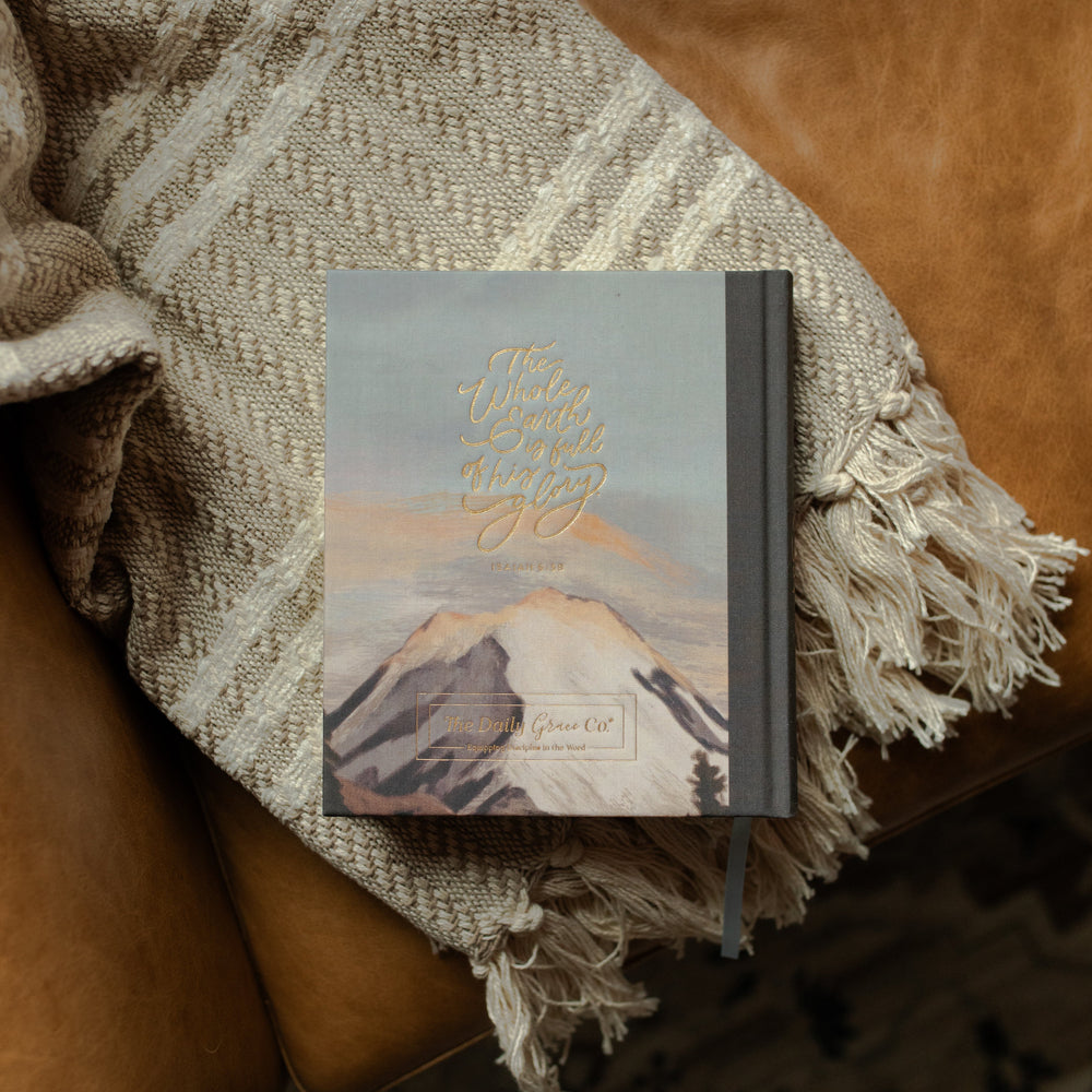 ESV Journaling Bible with mountains on the back cover with gold lettering on a blanket on a leather couch