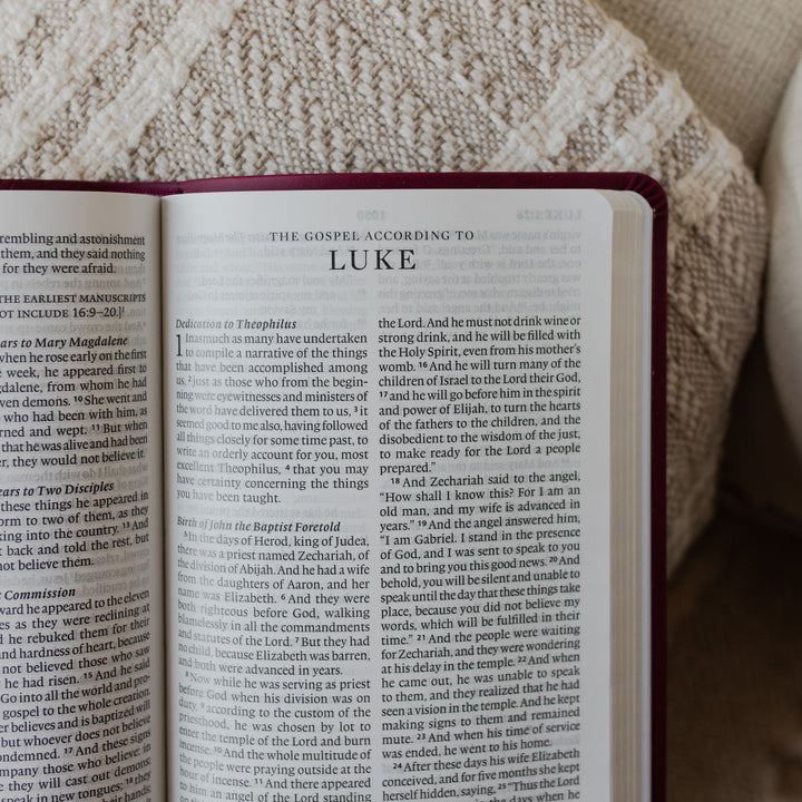The ESV Large Print Raspberry Bible opened to the beginning of Luke up close on a blanket on the arm of a couch