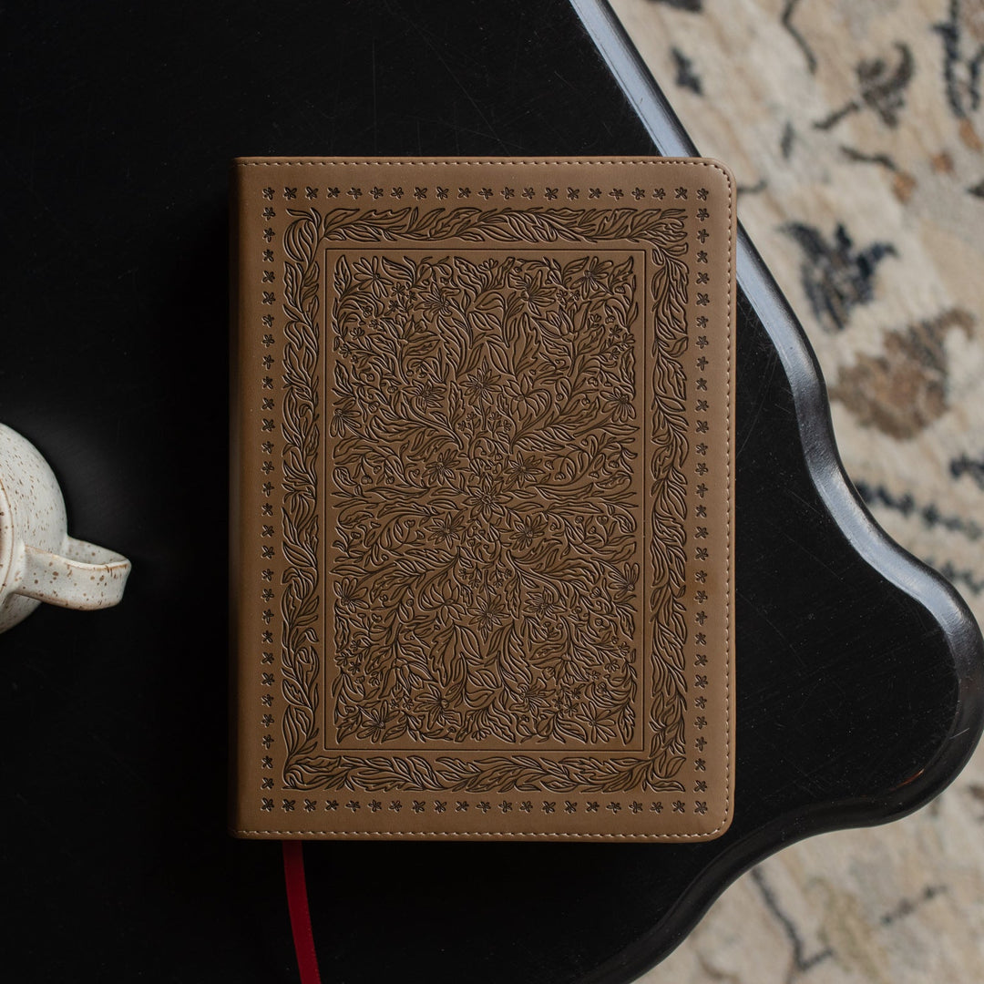 The ESV Single Column Journaling Bible with floral designs on a black wooden table near a coffee cup