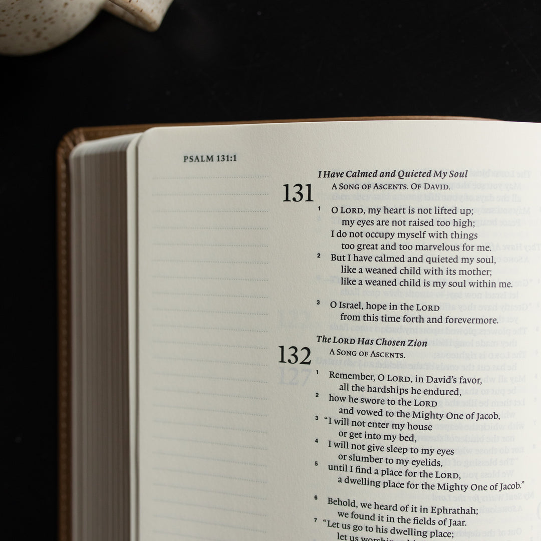The ESV Single Column Journaling Bible  opened to Psalms 131:1 up close on a black wooden table near a coffee cup