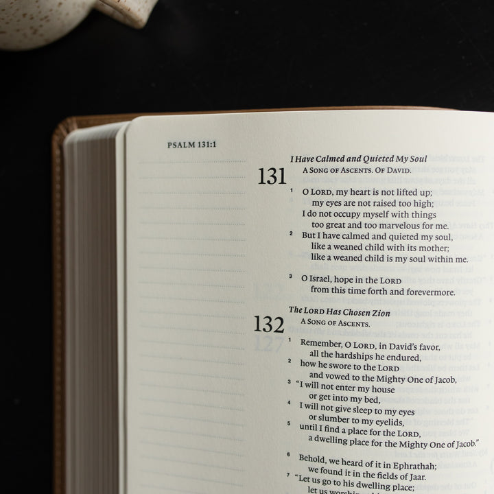 The ESV Single Column Journaling Bible  opened to Psalms 131:1 up close on a black wooden table near a coffee cup