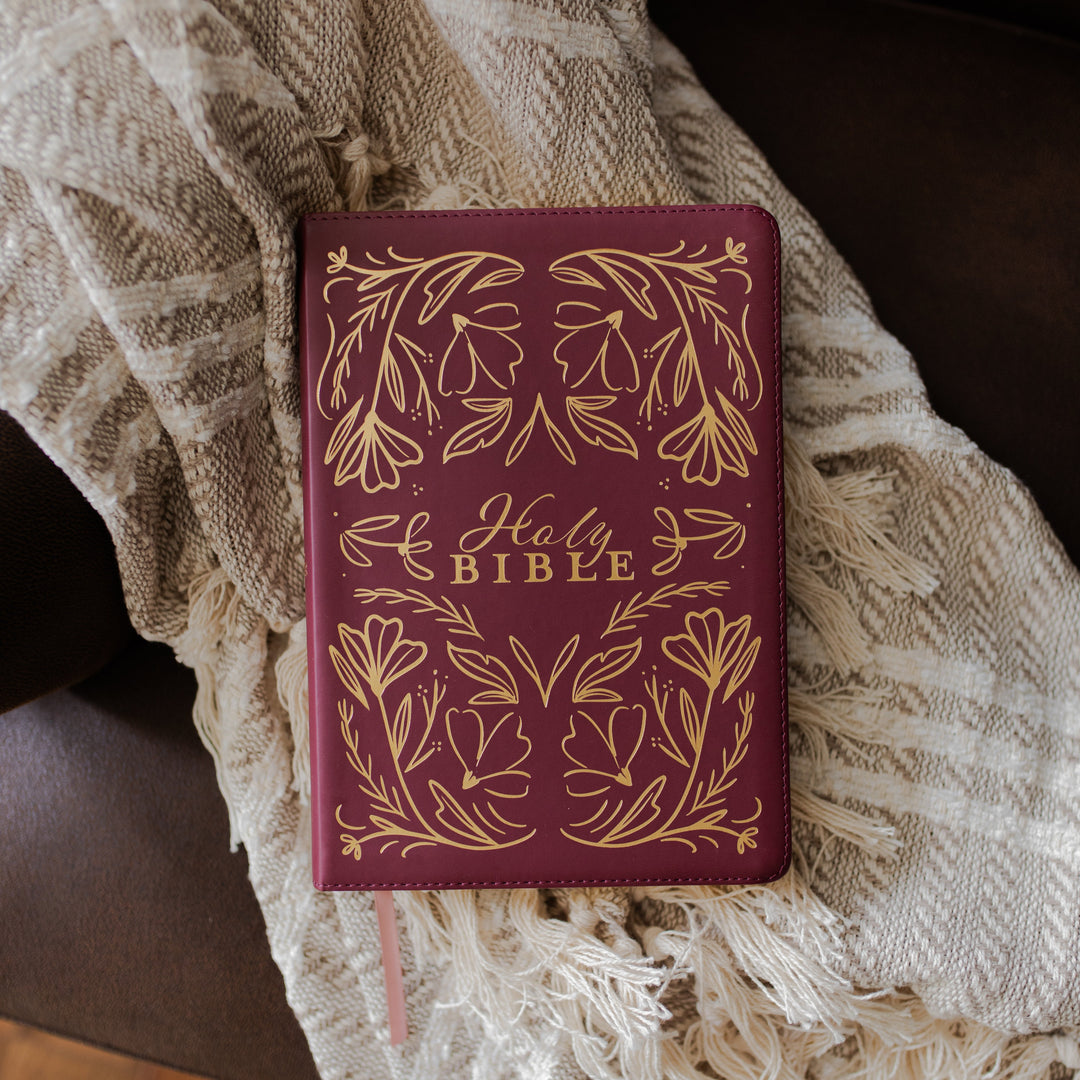 Maroon Bible with gold floral design on a textured blanket