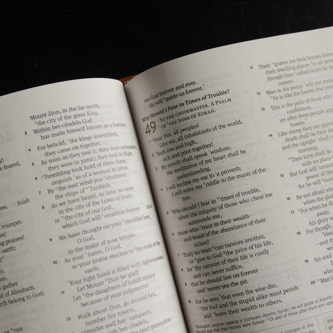 Up close of the top of A leather ESV bible opened to the Psalms pages on a dark wooden table