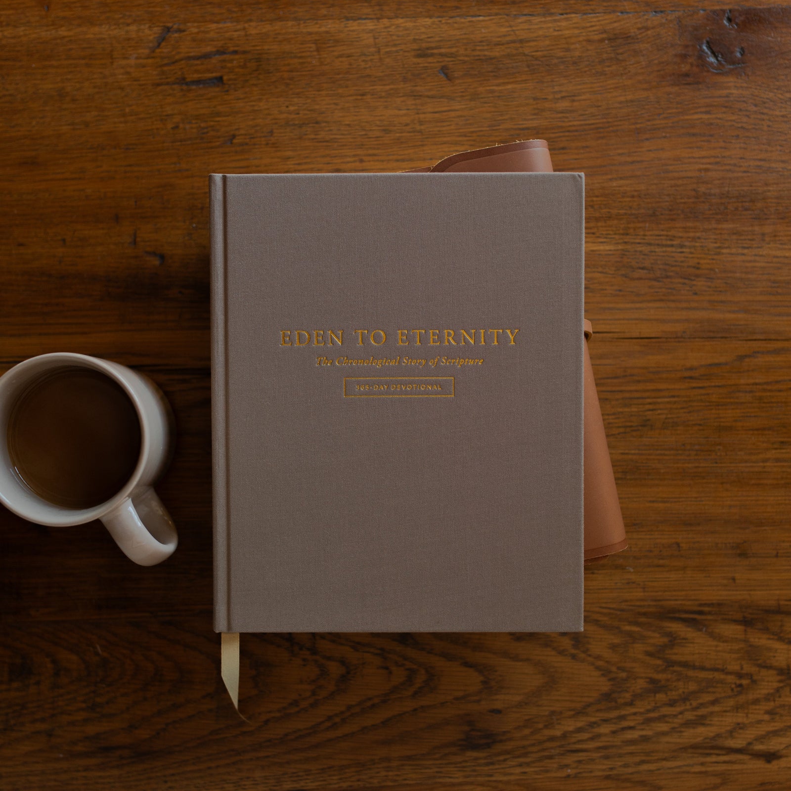 Eden to Eternity Devo cover on a leather wrapped bible next to a coffee cup on a wooden table