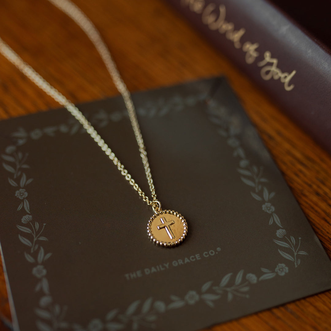 Embossed cross necklace on a wooden table next to a book