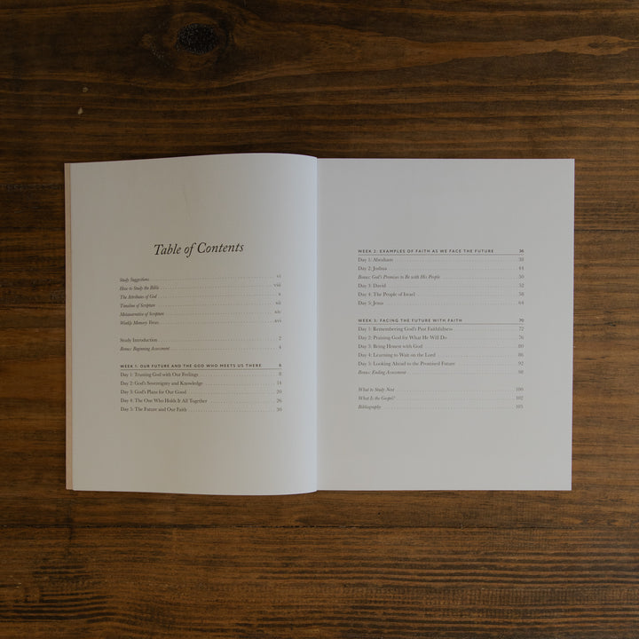 An open book showing a printed Table of Contents spread on a dark wood tabletop.