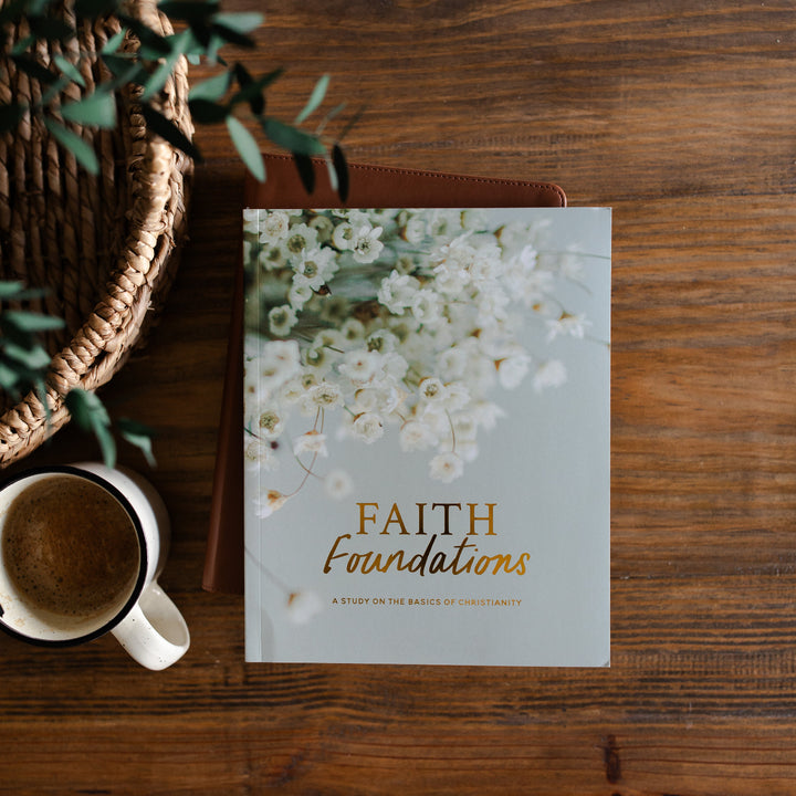 Faith Foundations Matte Study laying on a leather book next to a cup of coffee in a white mug; The study and the coffee is on a brown wooden table next to a hand woven basket