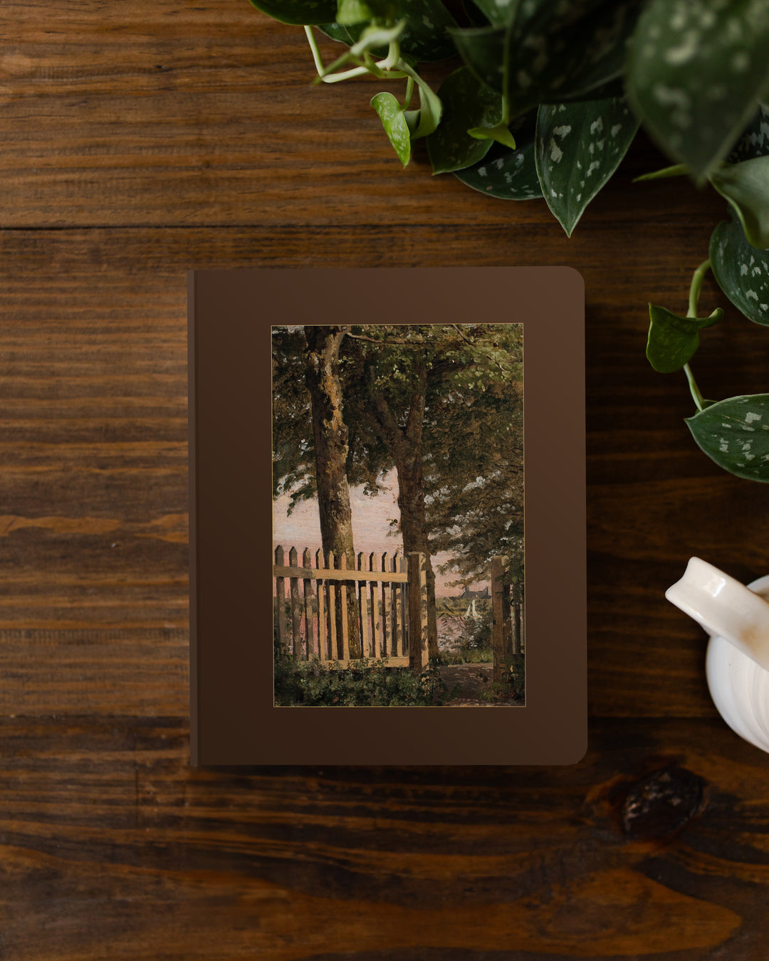Framed print of a forest scene on a bible with plants on a wooden table.