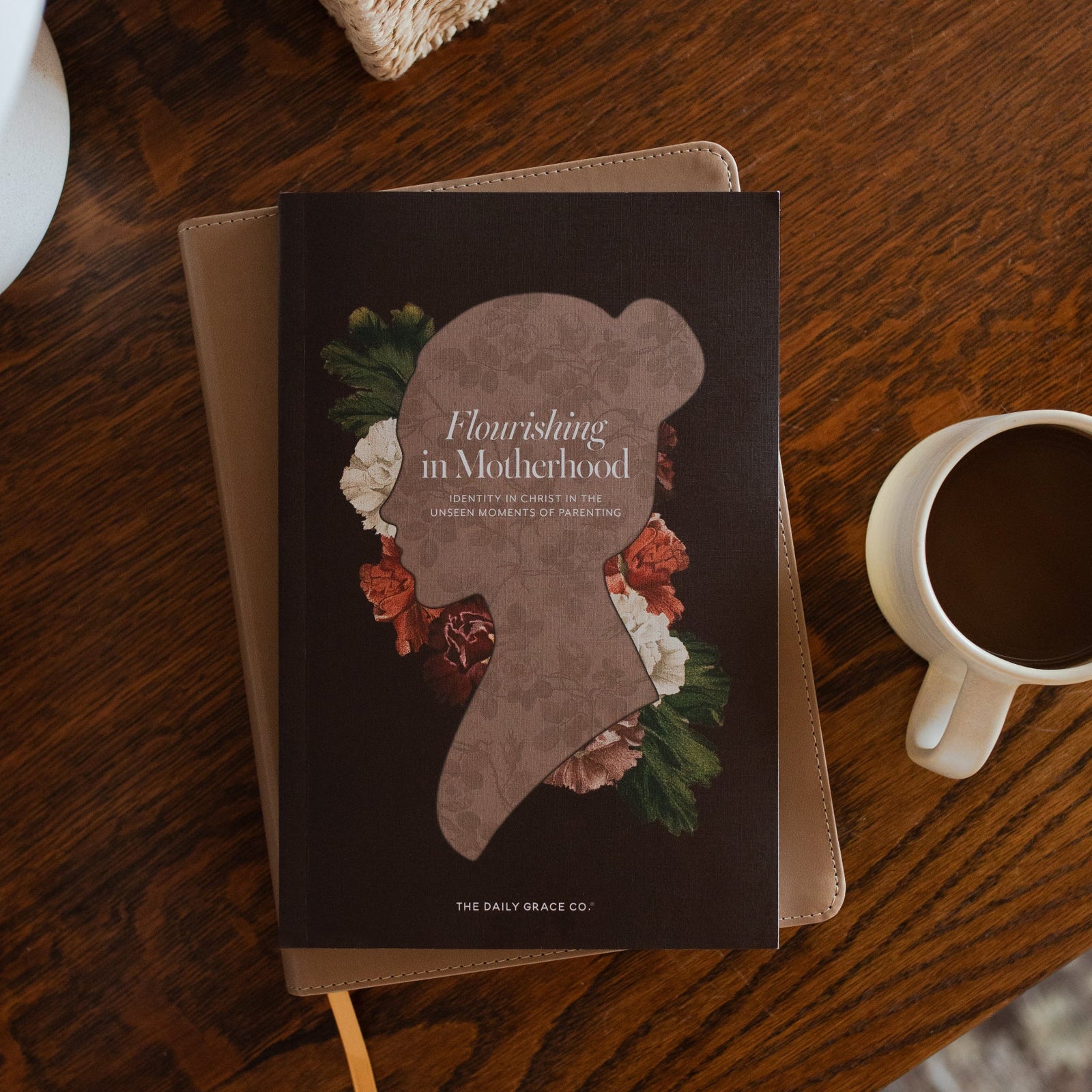 Flourishing in Motherhood Book cover on a closed bible on a wooden table near a coffee cup