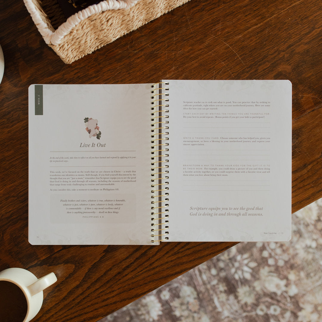 Flourishing in Motherhood spiral study opened to the Live it Out page on a wooden table near a coffee cup