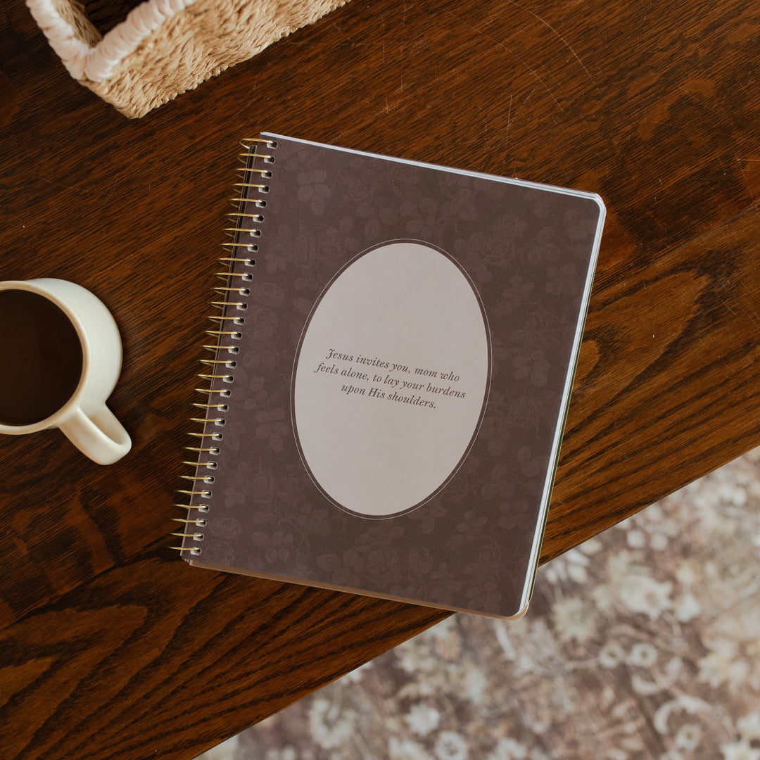 Flourishing in Motherhood spiral study opened to a small devotional page on a wooden table near a coffee cup