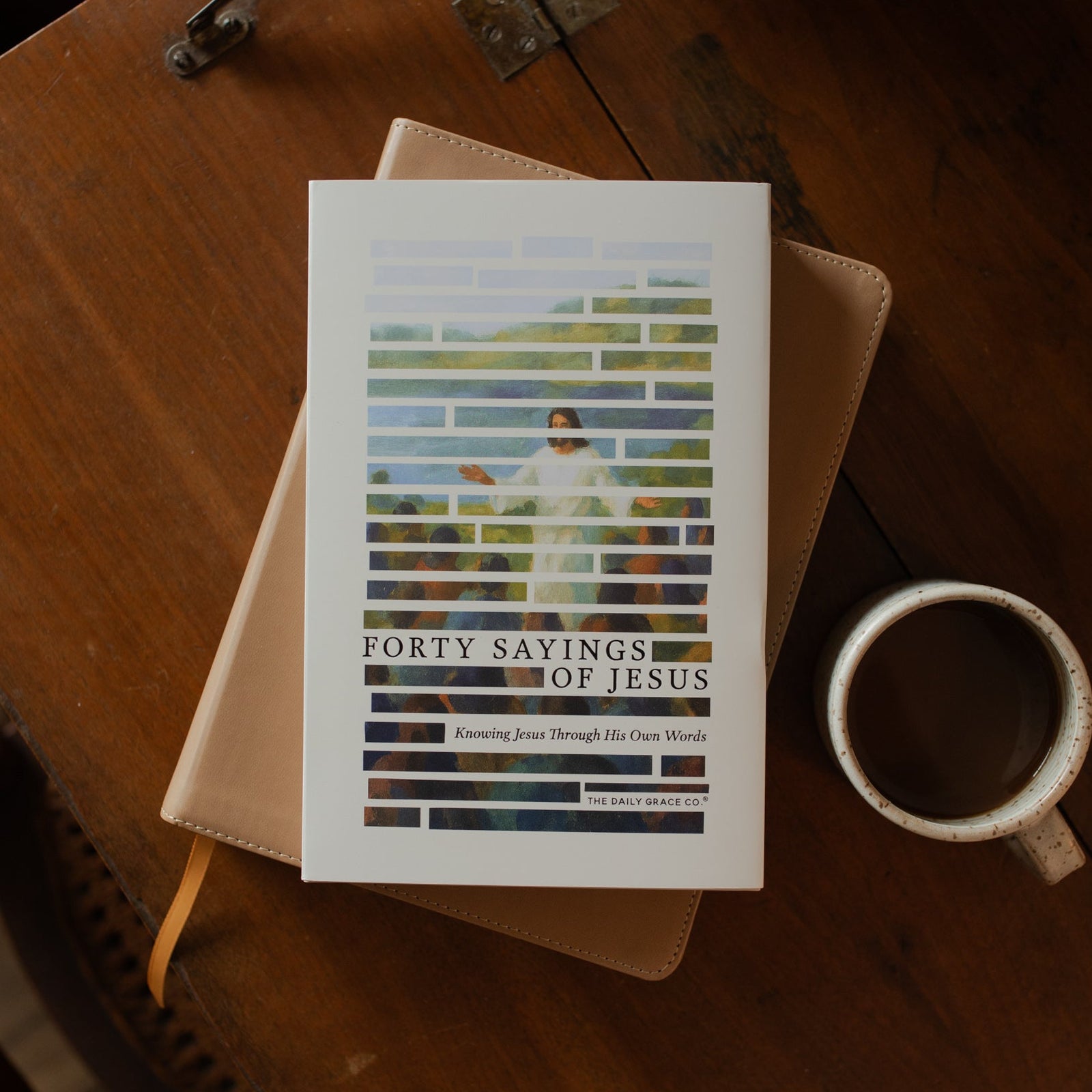 Forty Sayings of Jesus hardcover cover on a closed bible near a coffee cup on a wooden table